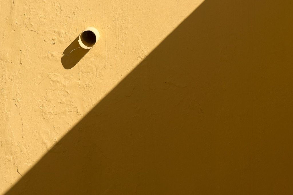 A sunlit yellow wall with a pipe casting a shadow, highlighting its texture.