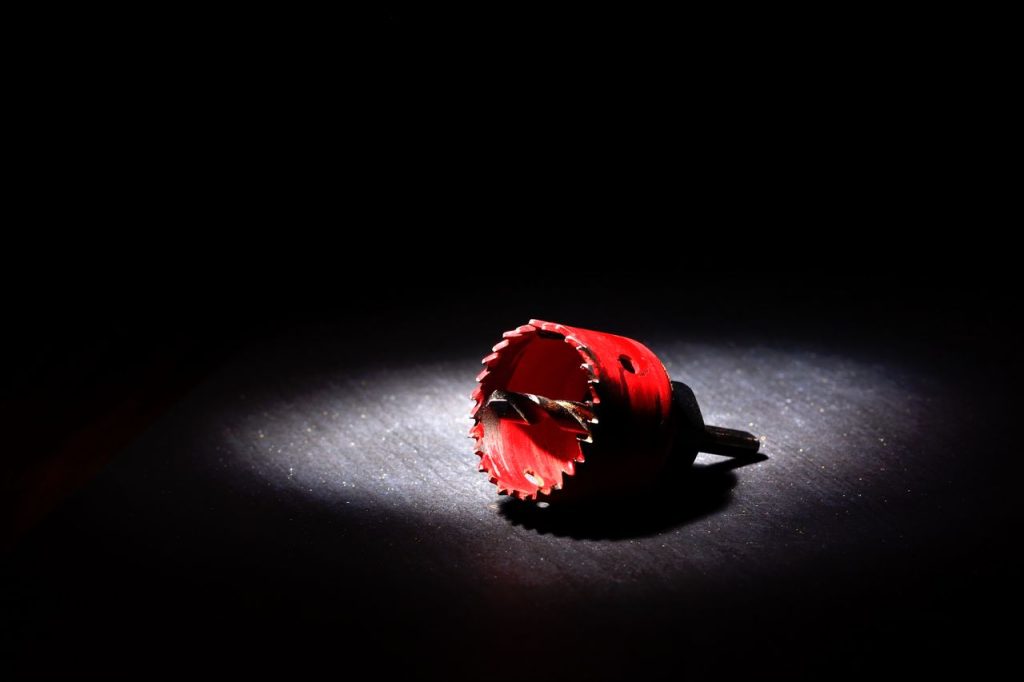Dramatic shot of a red hole saw tool illuminated against a black background in studio lighting.
